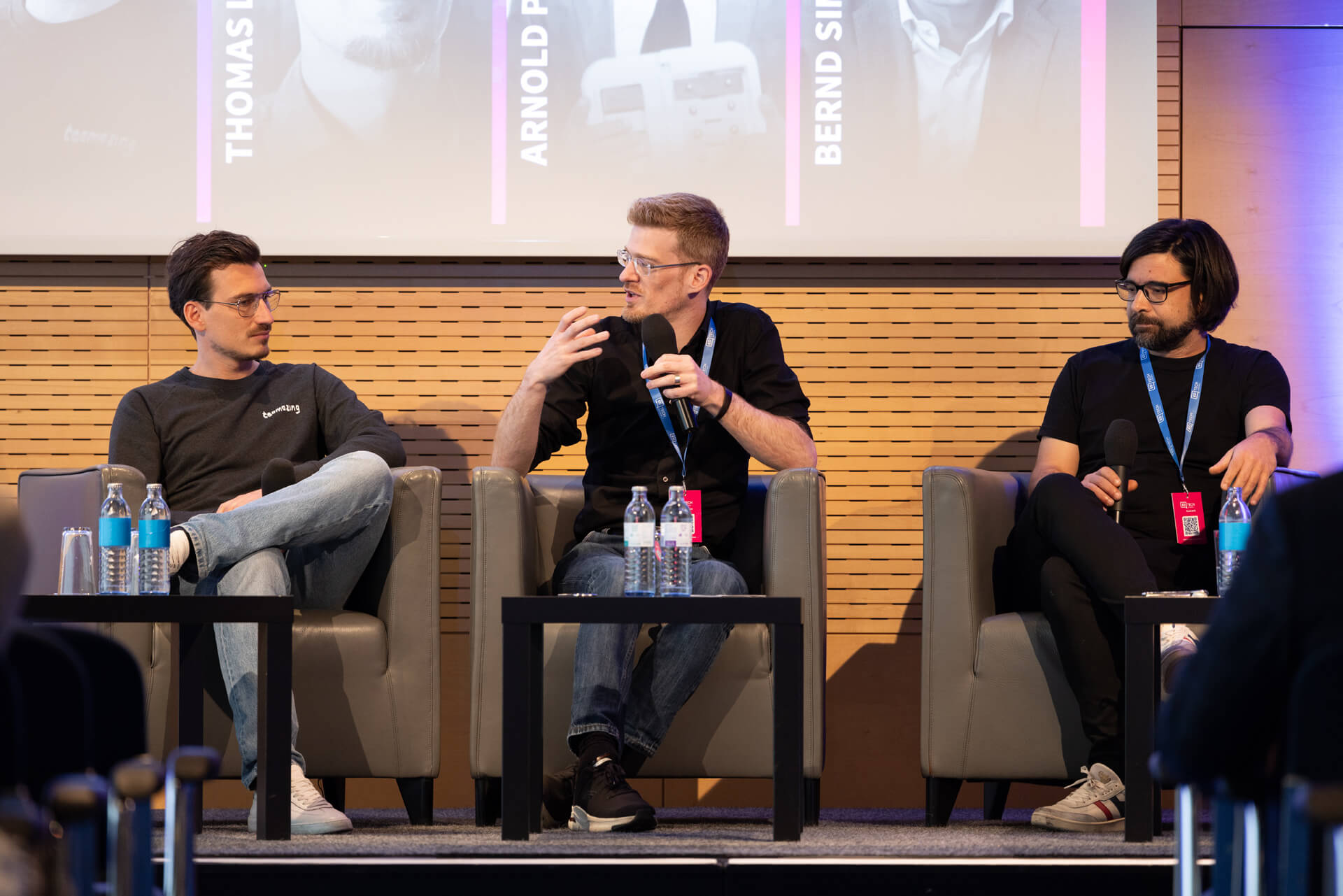 Drei Personen diskutieren bei einer Podiumsrunde auf einer Bühne.